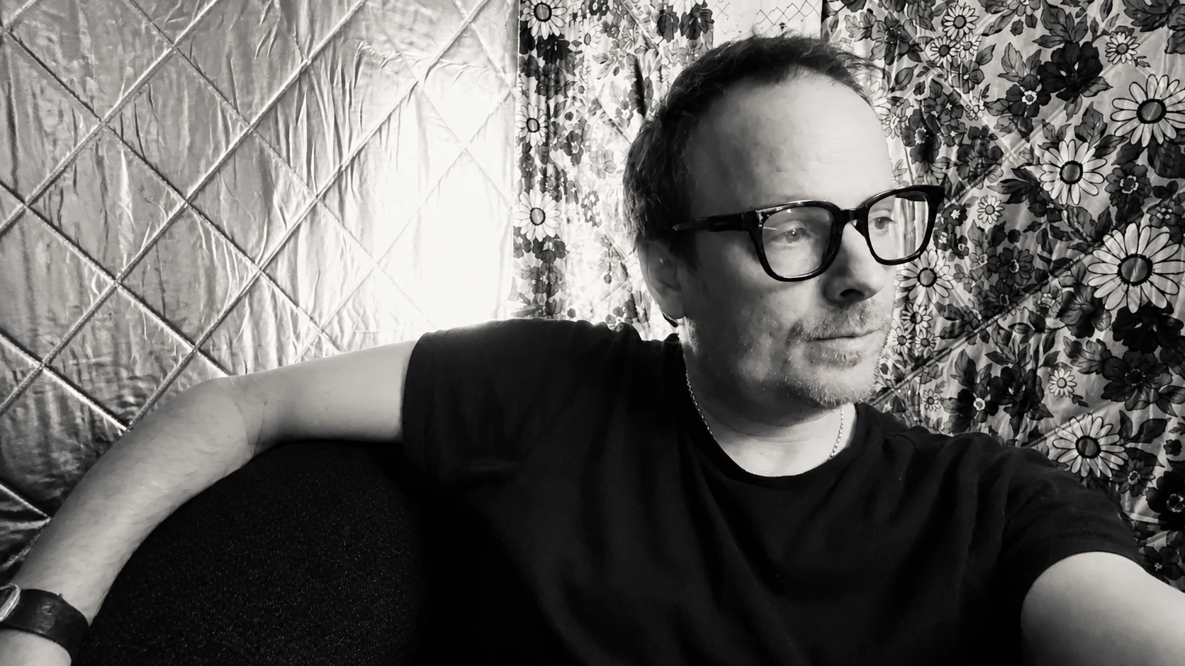Black-and-white portrait of John N. Farmer wearing glasses in front of reflective and floral backdrops.